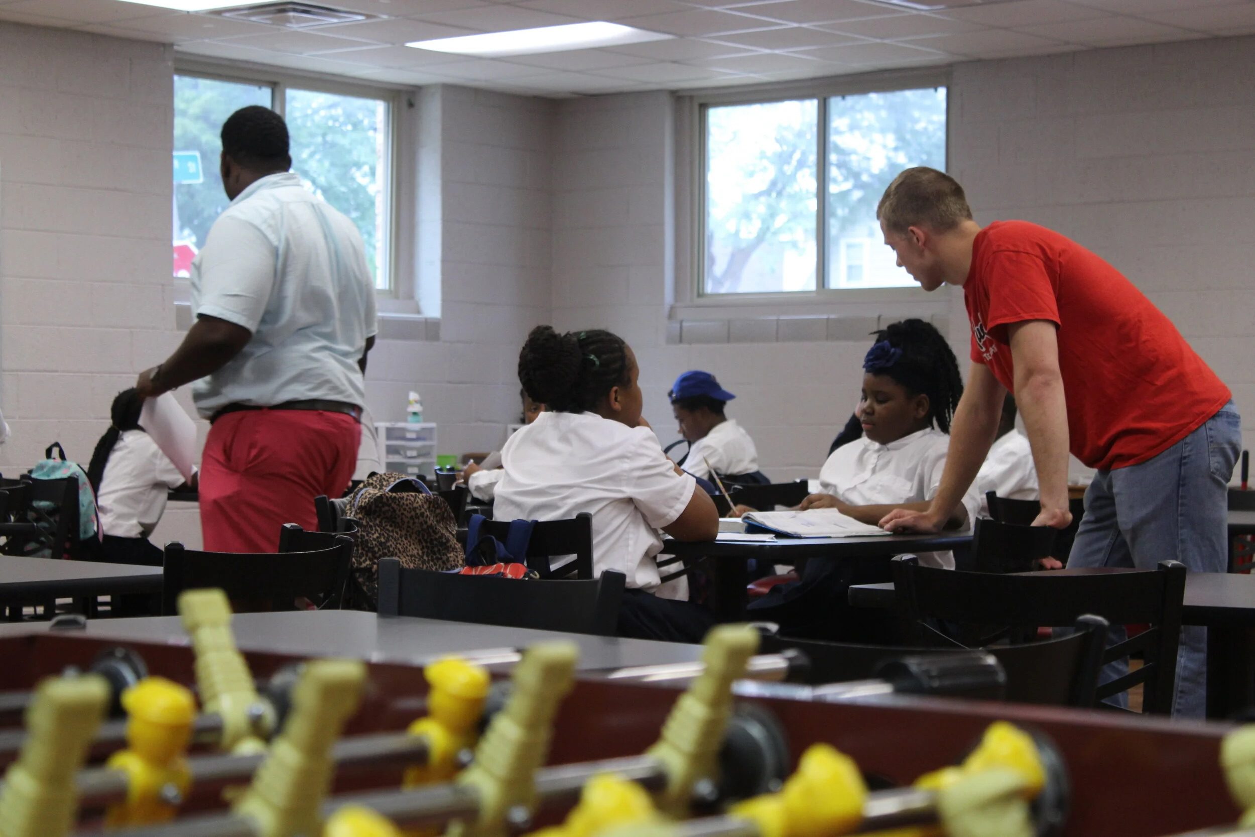 Students and staff work together at tables in a classroom workshop.